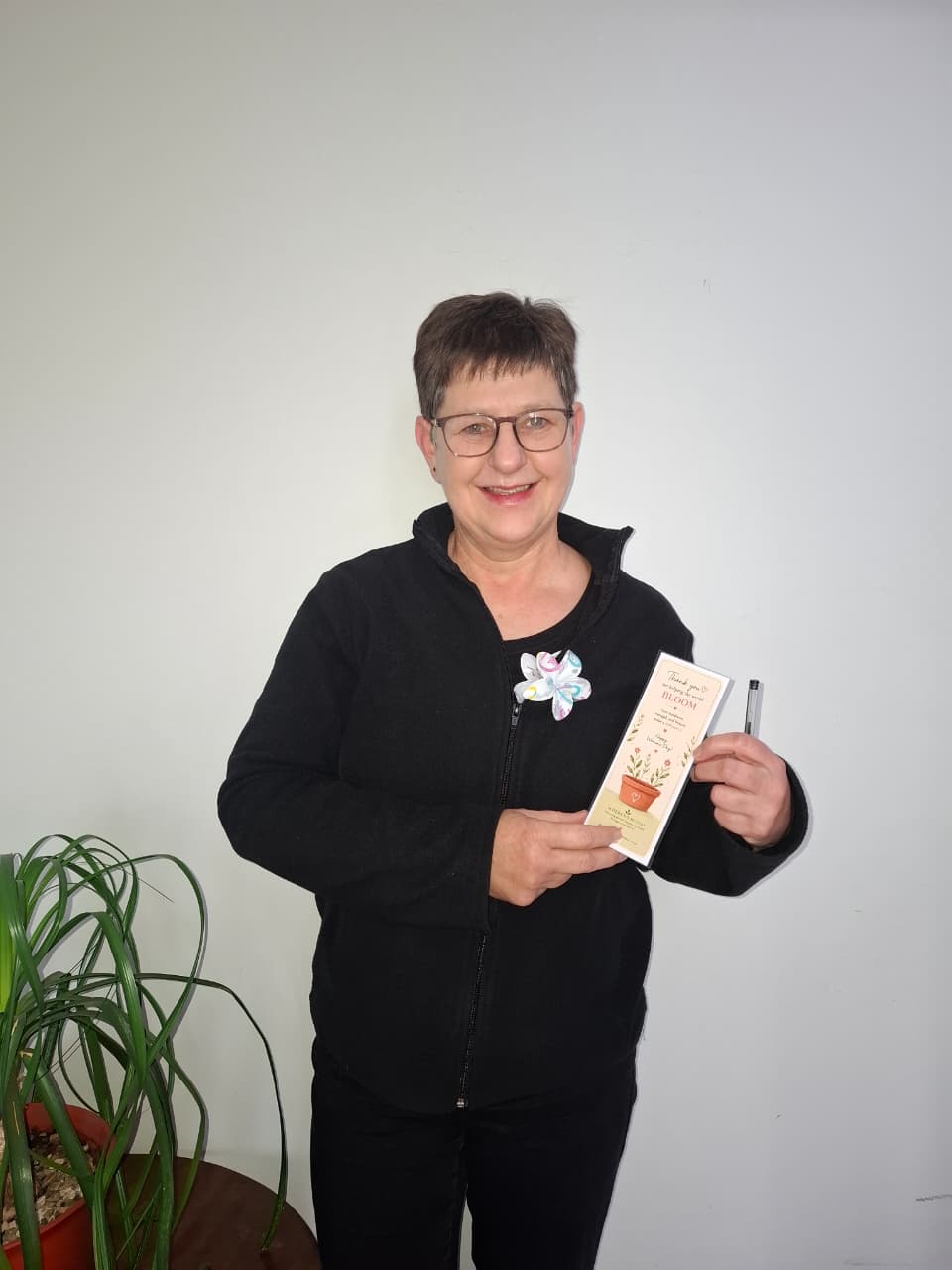 A Where We Bloom team member holding a 'Thank you for helping us Bloom' Women's Day card and pen.