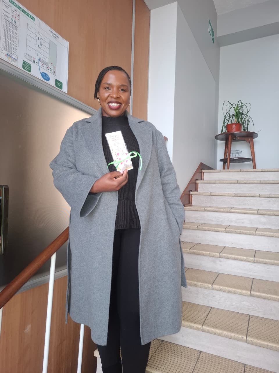A social worker smiling on the stairwell, holding her Women's Day thank-you card and flower hair clip.